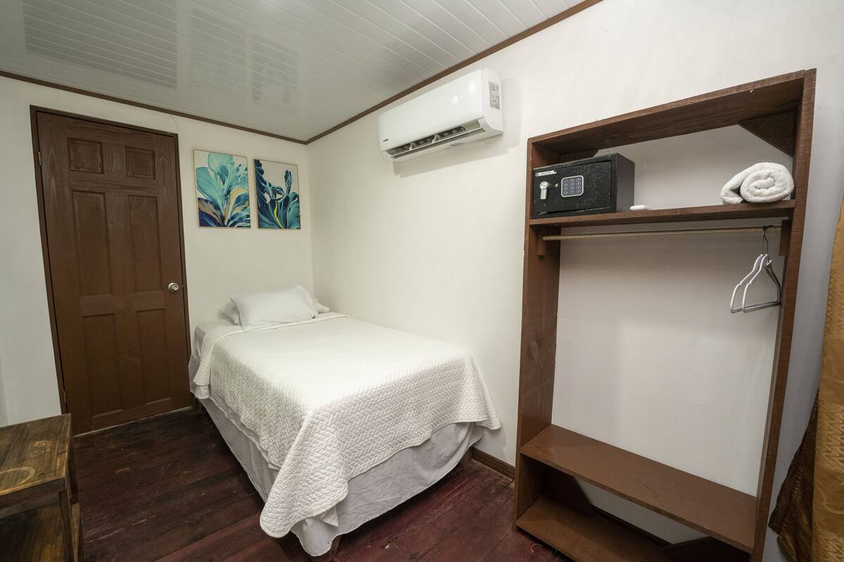 A bedroom with a bed, a wooden wardrobe, an air conditioning unit, and artwork on the wall.