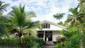 Un edificio con entrada cubierta, rodeado de abundante vegetación y palmeras.