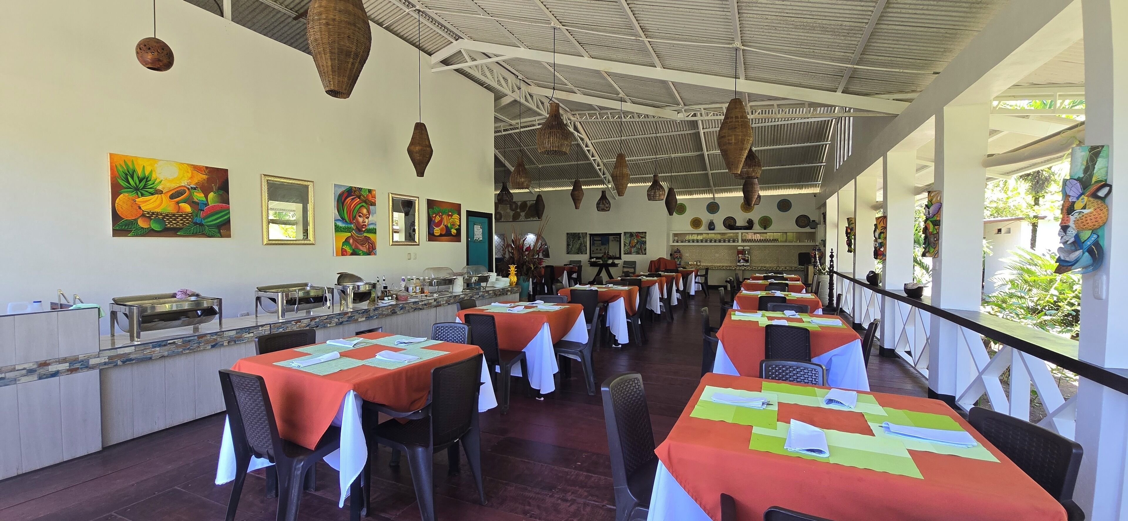Ein Restaurant mit orangefarben gedeckten Tischen, einer Küche und Bildern an den Wänden.