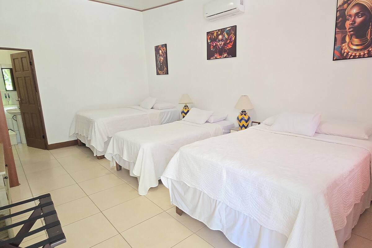 A hotel room with three single beds, a desk, and a chair. There are two wall-mounted lamps and a window with curtains.