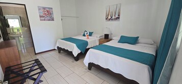 Habitación de hotel con dos camas, una mesita de noche con lámpara, un lavamanos pequeño y una silla de madera.