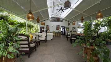 Un espacio interior amplio con techos altos, que incluye una sala de estar con sofás y sillones, rodeada de diversas plantas en macetas.