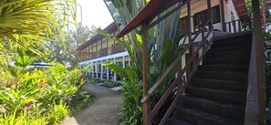 A pathway leading to a building with a wooden staircase and a balcony.