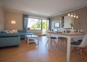 Relax in a spacious living area with a sofa, dining space with a table and chairs, and a large window offering a view of the outdoors.