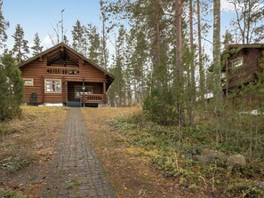 Puuinen mökki, jonka edessä on kivetty kulkuväylä, ja jonka ympärillä kasvaa puita.