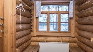 Interno di una baita di legno, con una panca, un termosifone e una finestra con tende.