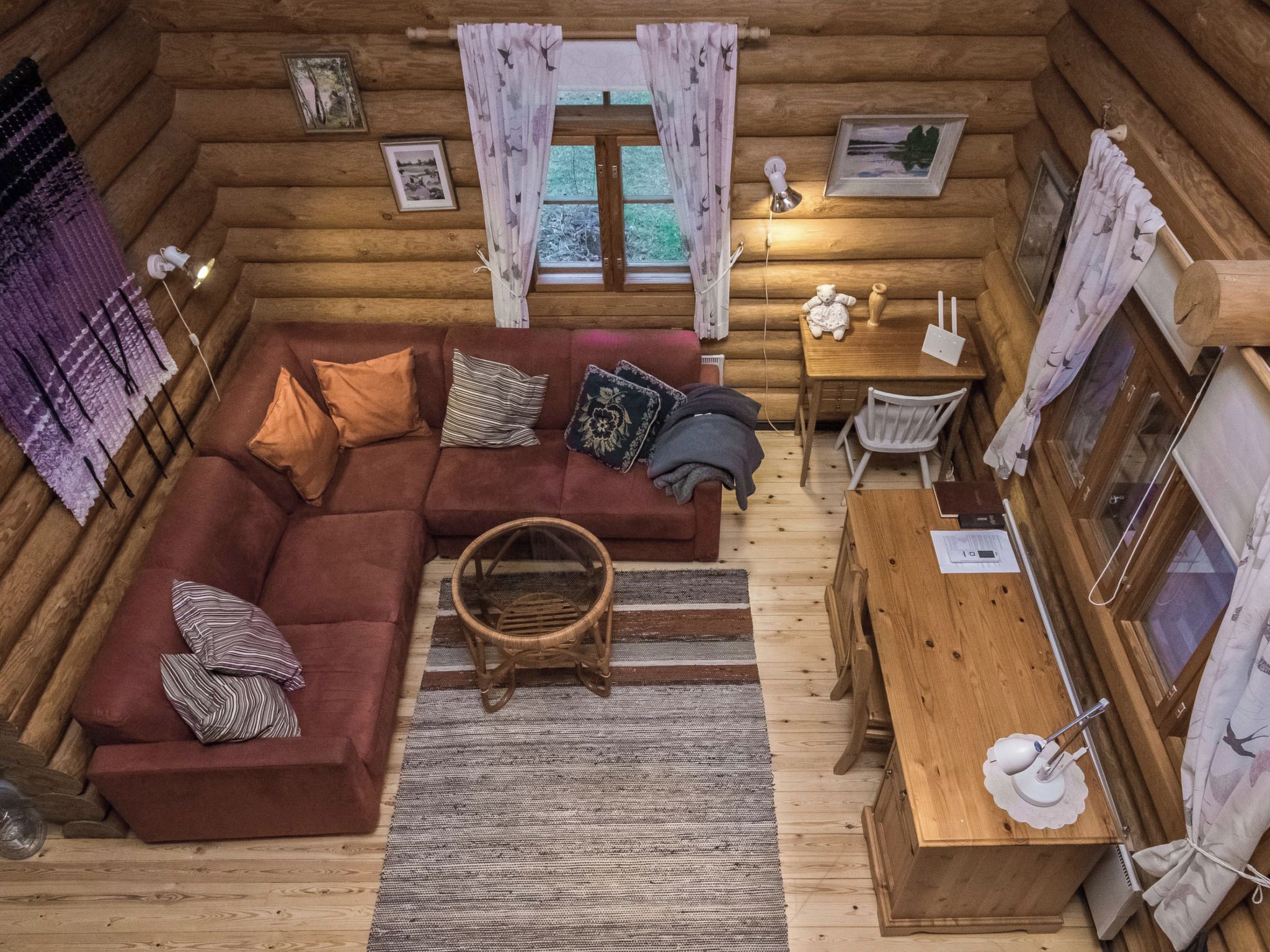 Un interior acogedor de cabaña de madera con un sofá seccional, una mesa de comedor y una cesta de mimbre.
