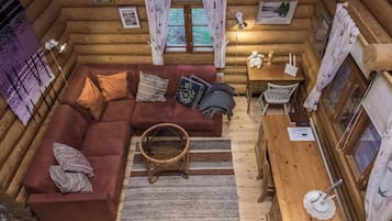 Un interior acogedor de cabaña de madera con un sofá seccional, una mesa de comedor y una cesta de mimbre.