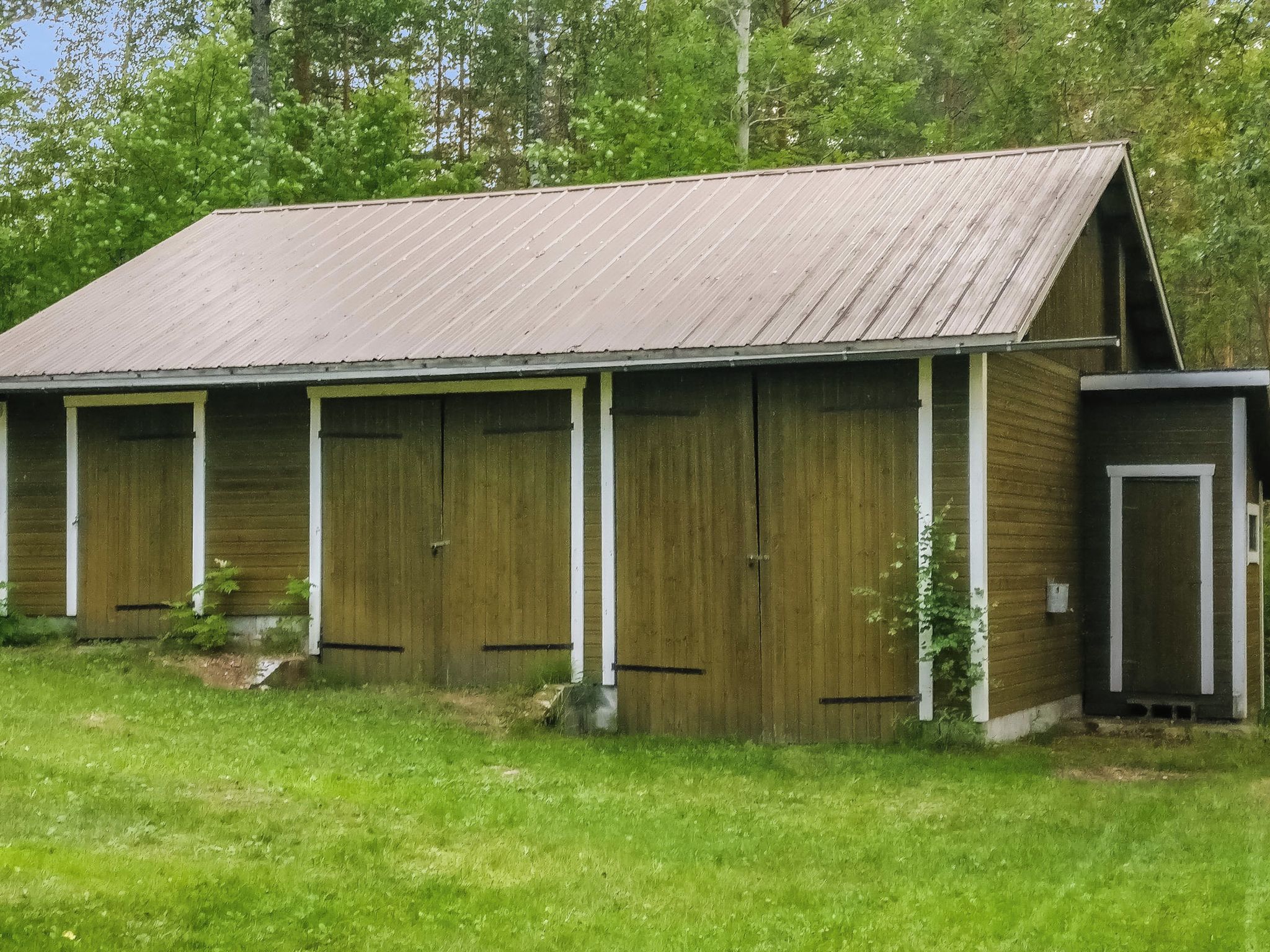 A rustic barn with a sloped roof, multiple large doors, and a small attached structure.