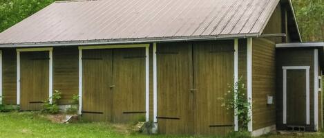 A rustic barn with a sloped roof, multiple large doors, and a small attached structure.