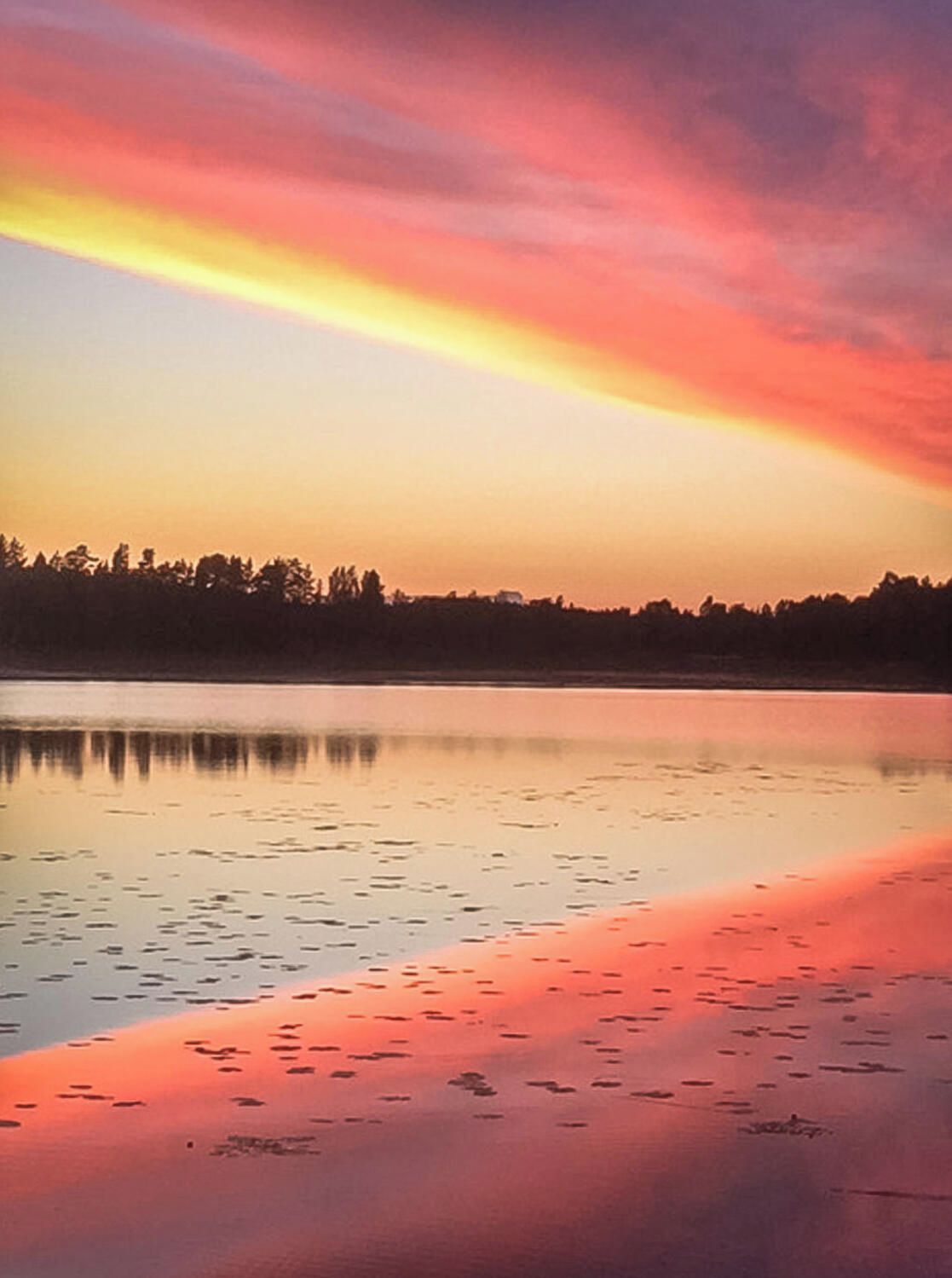 A calm body of water reflecting a sunset sky with a horizon line.