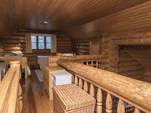 L’intérieur d’une cabane en rondins, avec un escalier en bois, un coin repas et une fenêtre avec des rideaux.