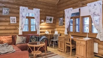 Ein gemütliches Blockhäuschen-Interieur mit Holzvertäfelung, einer Couch, einem Esstisch, Stühlen, einem kleinen Teppich und gerahmten Bildern an den Wänden.