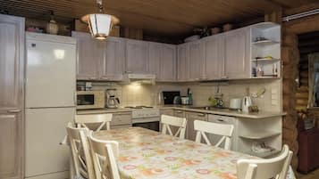 Cozinha compacta com armários brancos, uma mesa de jantar com toalha florida e um lustre.