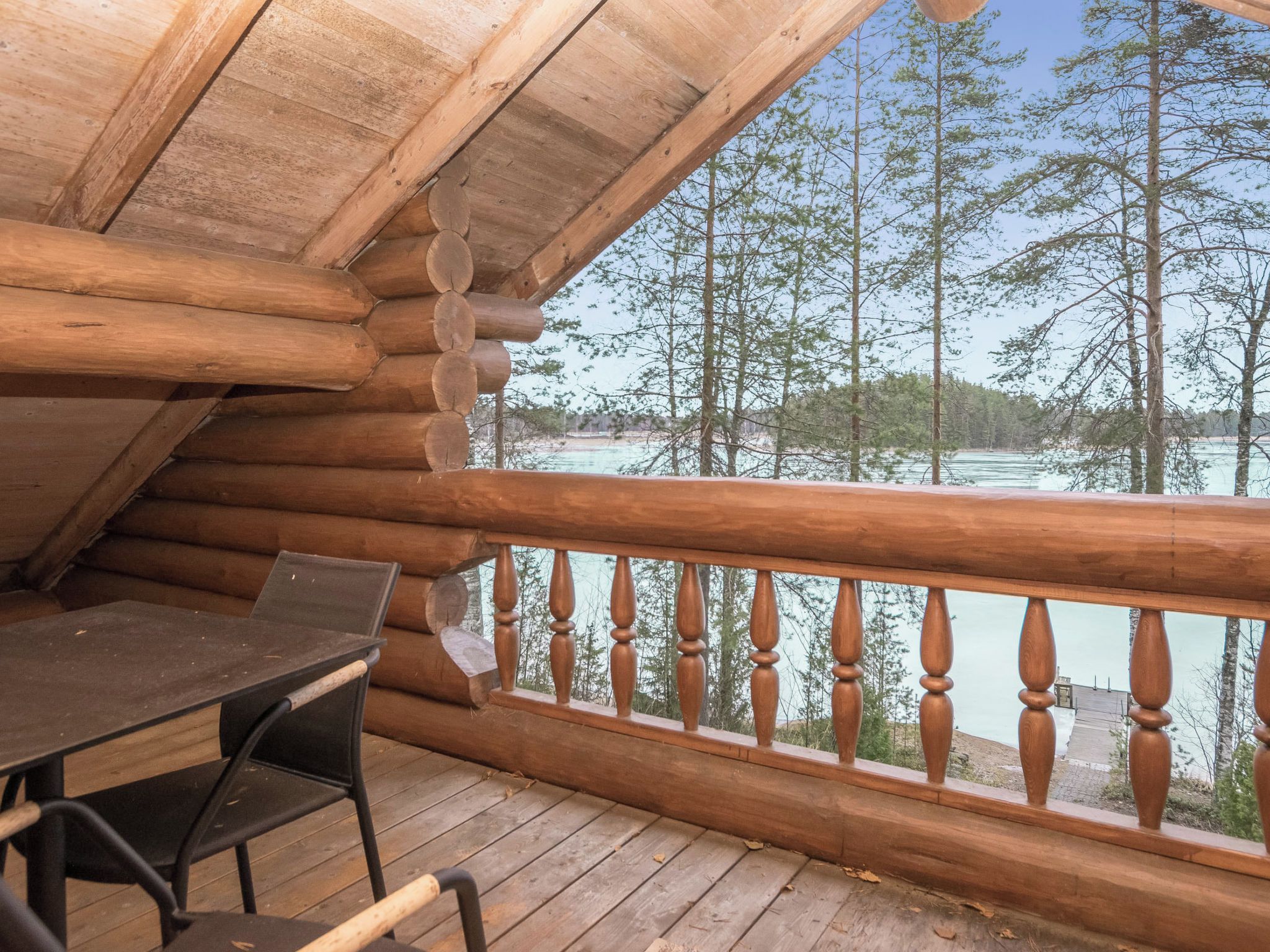 Una terraza de madera con una mesa y sillas, con vista a un cuerpo de agua y árboles.