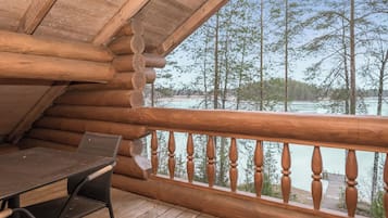 Una terraza de madera con una mesa y sillas, con vista a un cuerpo de agua y árboles.