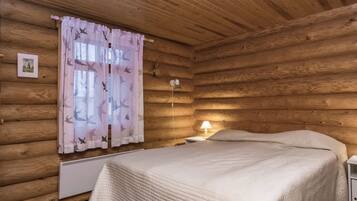 Quarto de cabana de madeira com uma cama, mesa de cabeceira, abajur e janela com cortinas.