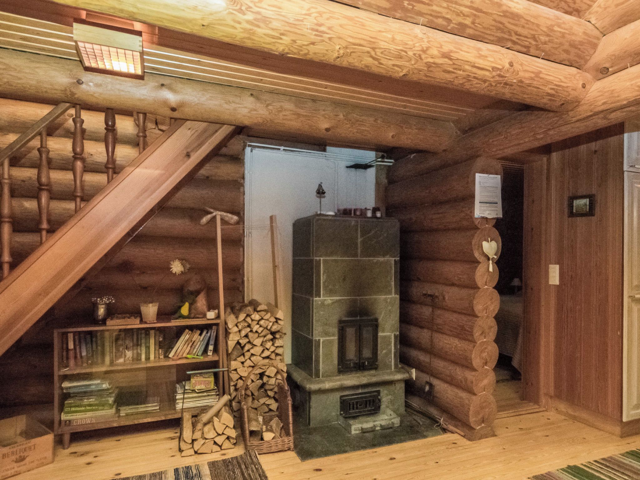 A log cabin interior with a wooden staircase, a fireplace, a bookshelf, and a door.