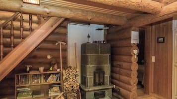 A log cabin interior with a wooden staircase, a fireplace, a bookshelf, and a door.
