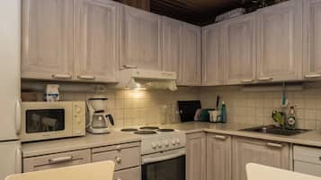 Una cocina con armarios blancos, estufa, microondas y cafetera.