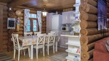 A cabin interior with a dining table, chairs, a refrigerator, a microwave, and a sink.