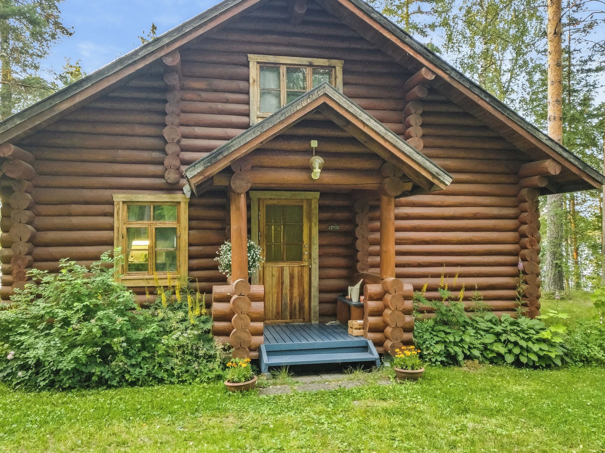 Hirsimökki, jossa on kuisti, ovi ja kaksi ikkunaa.