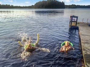 Järvi, jossa on laituri ja kaksi ihmistä kelluu vedessä.