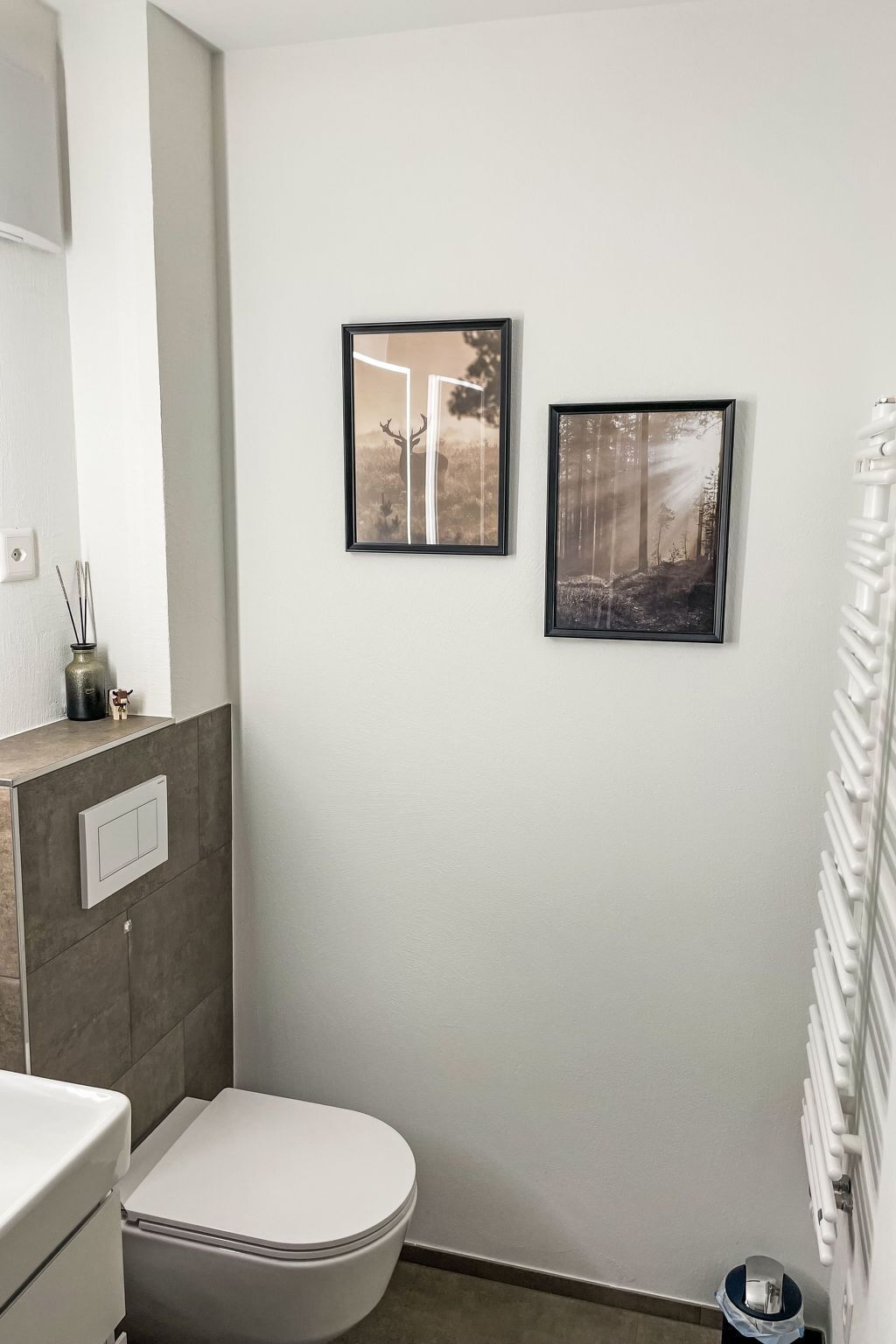 A bathroom with a toilet, a mirror, and two framed pictures on the wall.