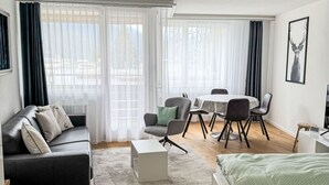 Una sala moderna con un sofá de cuero negro, una mesa de centro blanca, una mesa de comedor con sillas y una cama con ropa de cama verde.