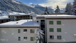 Un edificio moderno con múltiples ventanas y techo plano, rodeado de árboles cubiertos de nieve y montañas al fondo.