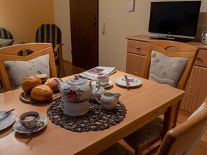 Comedor con una mesa de madera dispuesta para dos personas, que incluye tetera, tazas, platos y panecillos.