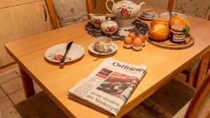 A breakfast setup with a teapot, cups, eggs, bread, and a newspaper on a wooden table. - Am Nordkap by Interhome (Norddeich)