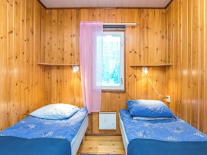 A cabin with two beds, a window with a curtain, and wall-mounted lights.