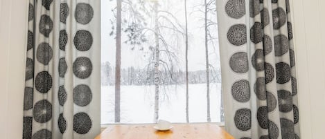 A room with a wooden table, a white hat on it, and a window with curtains featuring circular patterns.