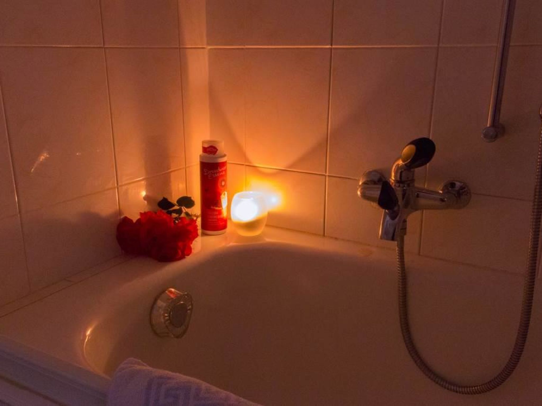 A bathroom with a bathtub, a shower, a bottle of shampoo, and a candle.