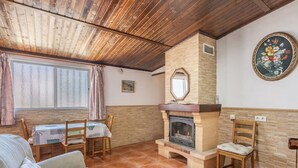Un salon chaleureux avec une cheminée, un plafond en bois et un coin repas comprenant une table et des chaises.
