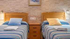 Une chambre avec deux lits, chacun doté d’une tête de lit en bois, d’une couvre-lit à rayures bleues et blanches et d’un oreiller. Un tableau encadré représentant des fleurs est accroché au mur, au-dessus des lits.