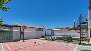 Un terrain de basket avec un panier, un ballon rouge et une piscine en arrière-plan.