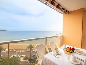 A balcony with a table set for breakfast, overlooking a beach and parking area.