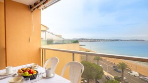 A balcony with a table set for breakfast, overlooking a coastal view with a beach and cityscape. - Le Capitole by Interhome (Fréjus)