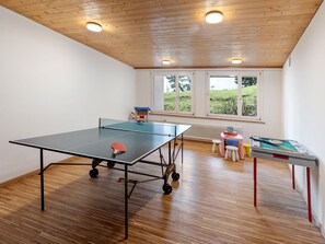 Ein Zimmer mit Pongtisch, Billardtisch und einem Fenster mit Blick auf Grünflächen.