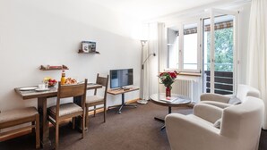 A modern living room with a dining area, a flat-screen TV, a round table with a vase of flowers, and a sofa. - Parkareal Apt 601 by Interhome (Davos)