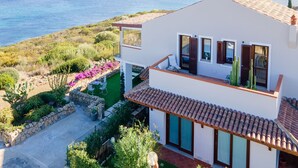 Ein modernes, zweistöckiges Haus mit einem Balkon mit Blick auf eine Küstenlandschaft, einschließlich Meer und vorgelagerter Inseln.