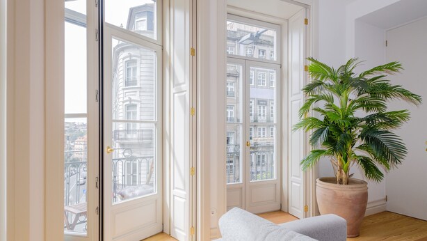 Een kamer met een groot raam, een potplant en een witte bank.