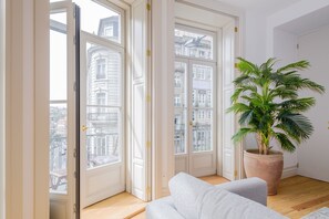 Een kamer met een groot raam, een potplant en een witte bank.