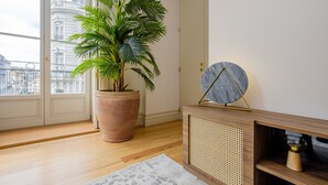 Een kamer met een grote potplant, een decoratief rond object op een console tafel, en een uitzicht op een gebouw door een glazen deur.