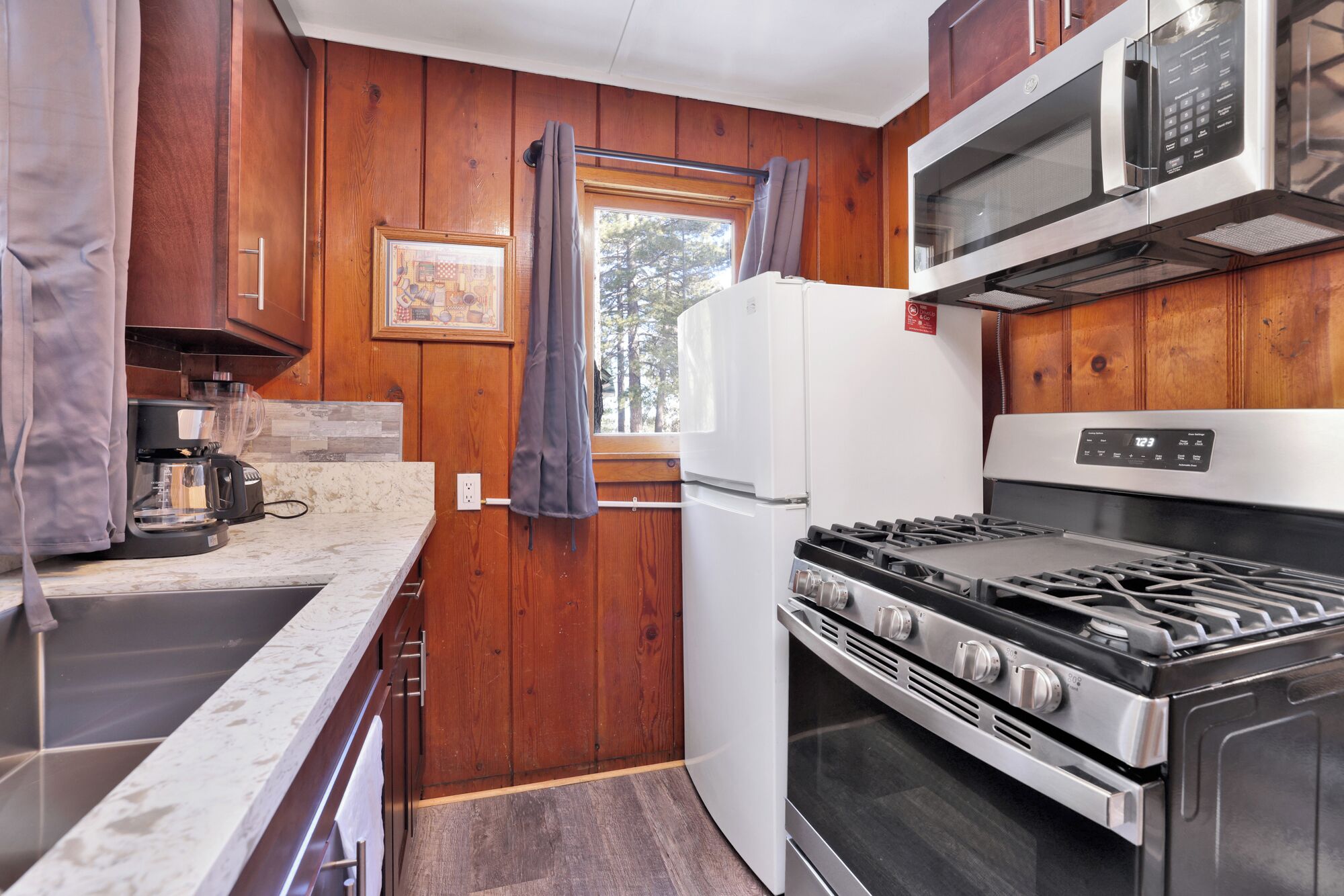 Une cuisine de taille réduite avec des murs en bois, un réfrigérateur blanc, une cuisinière et un four à micro-ondes.