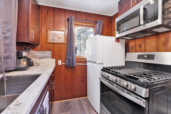 A compact kitchen with wooden walls, a white refrigerator, a stove, and a microwave. - Little Pines #102 (Big Bear Lake)