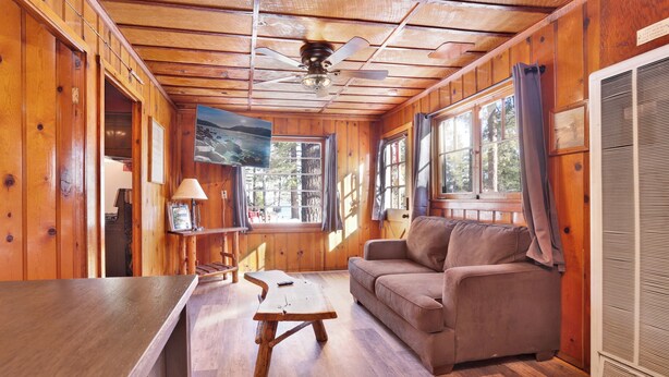 A cabin interior with a wooden floor, a sofa, a table, and a ceiling fan. - Little Pines #102 (Big Bear Lake)
