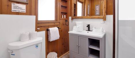 Une salle de bain équipée de toilettes, d’un lavabo et d’un miroir. Un panneau indique qu’il est interdit de jeter les couches, les essuie-tout et les produits d’hygiène féminine dans les toilettes.